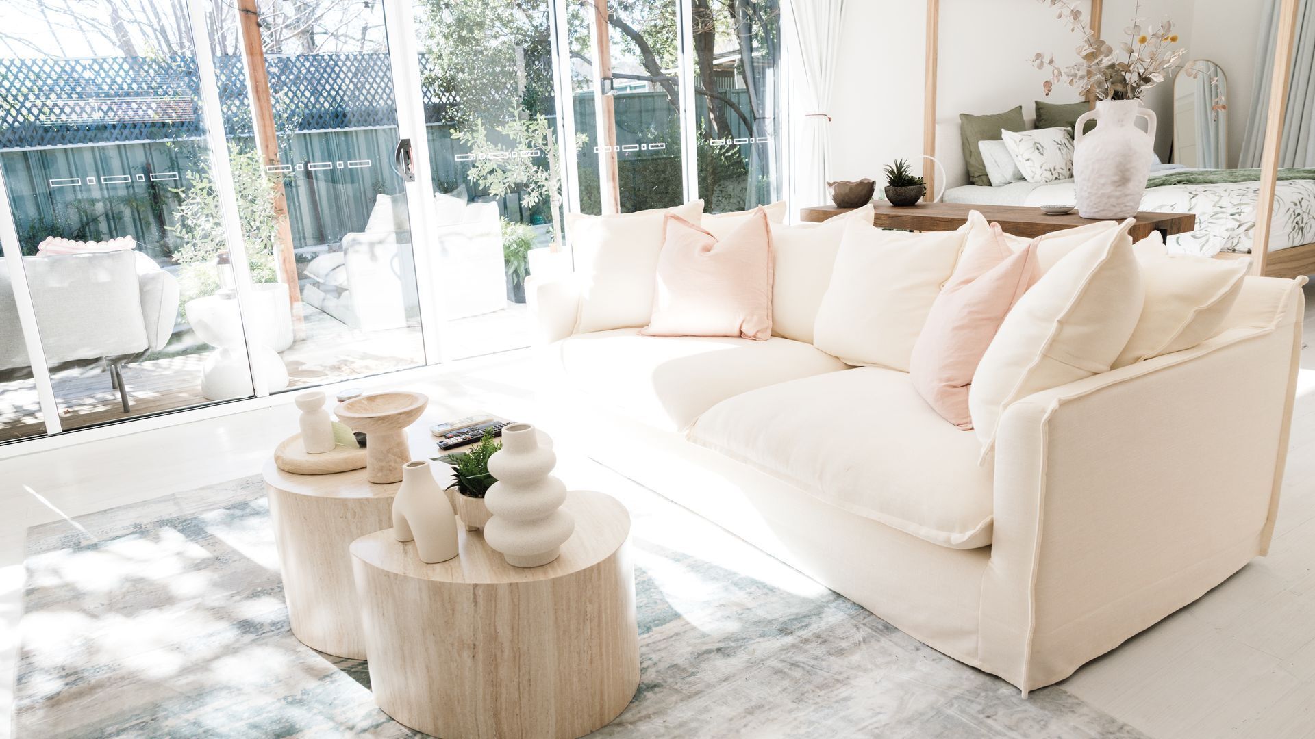 A modern living room with a white sofa, round wooden side tables, and a large glass window.