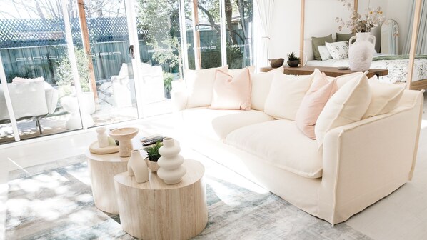 A modern living room with a white sofa, round wooden side tables, and a large glass window.