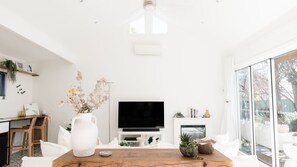 A modern living room with a wooden coffee table, a white vase with dried flowers, a flat-screen TV, and a fireplace.