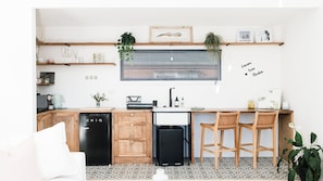 A modern kitchen with wooden cabinets, a black dishwasher, a sink, and a bar area with two wooden stools.