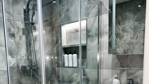 Une salle de bain moderne avec une douche en verre, un lavabo blanc et un mur recouvert de carreaux de marbre.