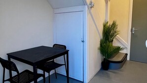 Une petite pièce avec une porte blanche, une table noire avec deux chaises, une plante en pot et un escalier.