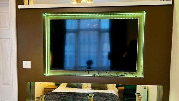 Un téléviseur fixé au mur, avec une étagère en dessous.