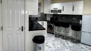 Une cuisine moderne avec des armoires blanches, un comptoir noir, une poubelle en acier inoxydable, un lave-linge et une horloge murale.