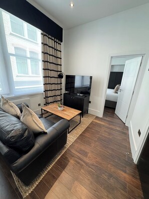 Ein modernes Wohnzimmer mit einer schwarzen Ledersofa, einem Holztisch, einem Fernseher und einem Bücherregal.