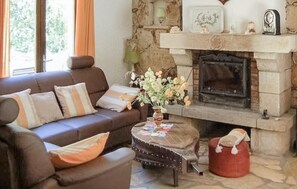 Ein Wohnzimmer mit einem braunen Sofa, einem kleinen Tisch mit Blumenvase, einem Kamin und einer Steinwand.