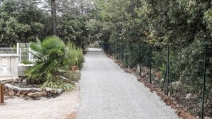 A gravel pathway flanked by greenery and a fence, leading to a building with a stone base and a white structure. - Nice home in Regusse with private swimming pool, can be inside or outside (Regusse)