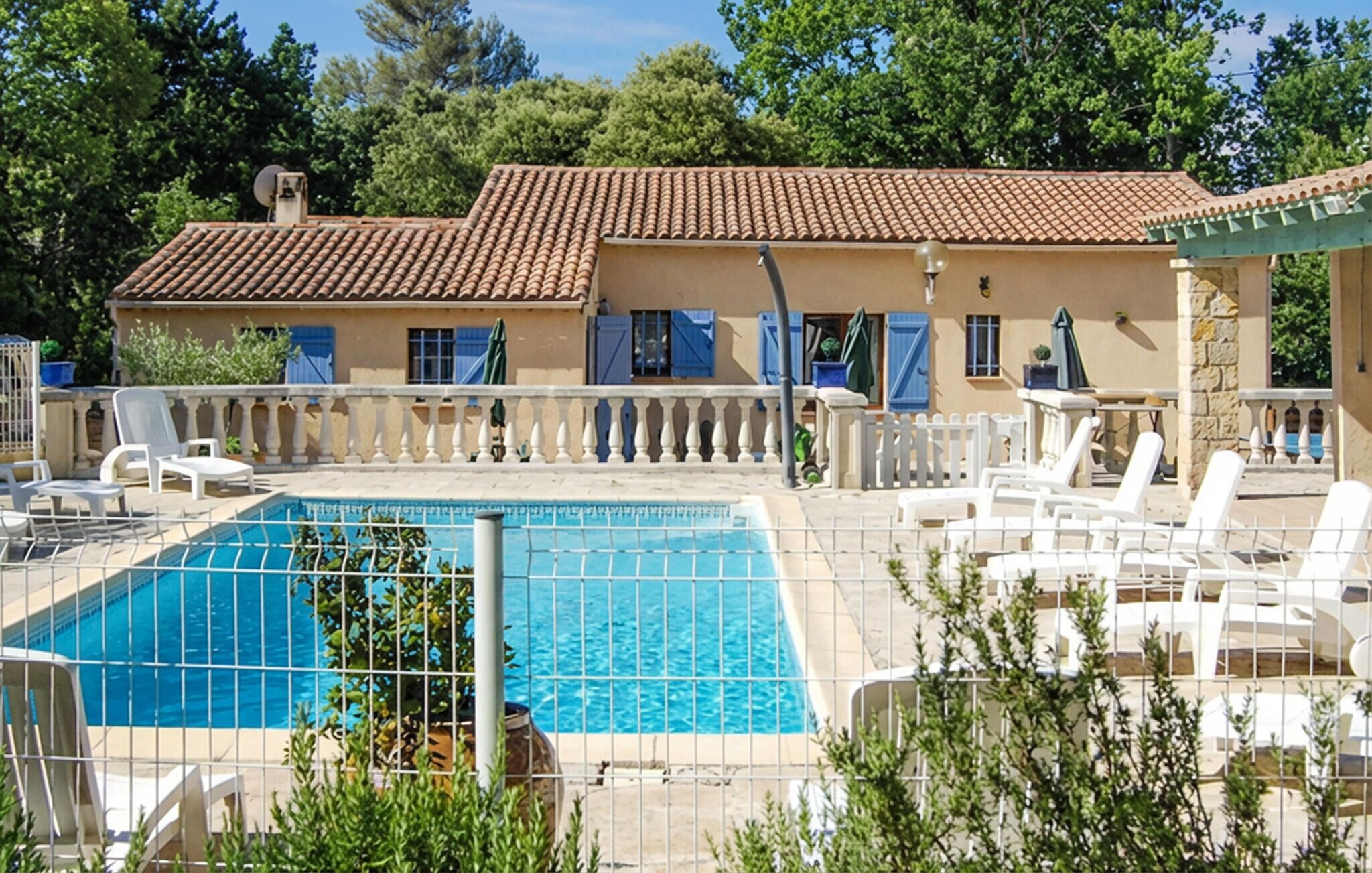A pool area with a tiled roof, white lounge chairs, and a fenced swimming pool.