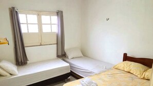 Ein Zimmer mit zwei Betten, einem Vorhangfenster, einem Deckenventilator und einer Klimaanlage.