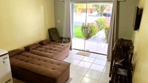 Ein Wohnzimmer mit Sofa, Sessel, Fernseher und Blick ins Freie.