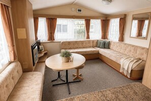 Ein gemütliches Wohnmobil-Interieur mit einer Eckcouch, einem runden Tisch und einem Fernseher.