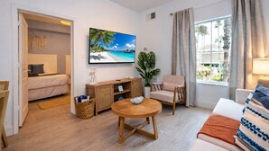 Ein modernes Wohnzimmer mit einem Bett, einem Fernseher, einem Couchtisch aus Holz, einem Sessel und einem Fenster mit Vorhängen.