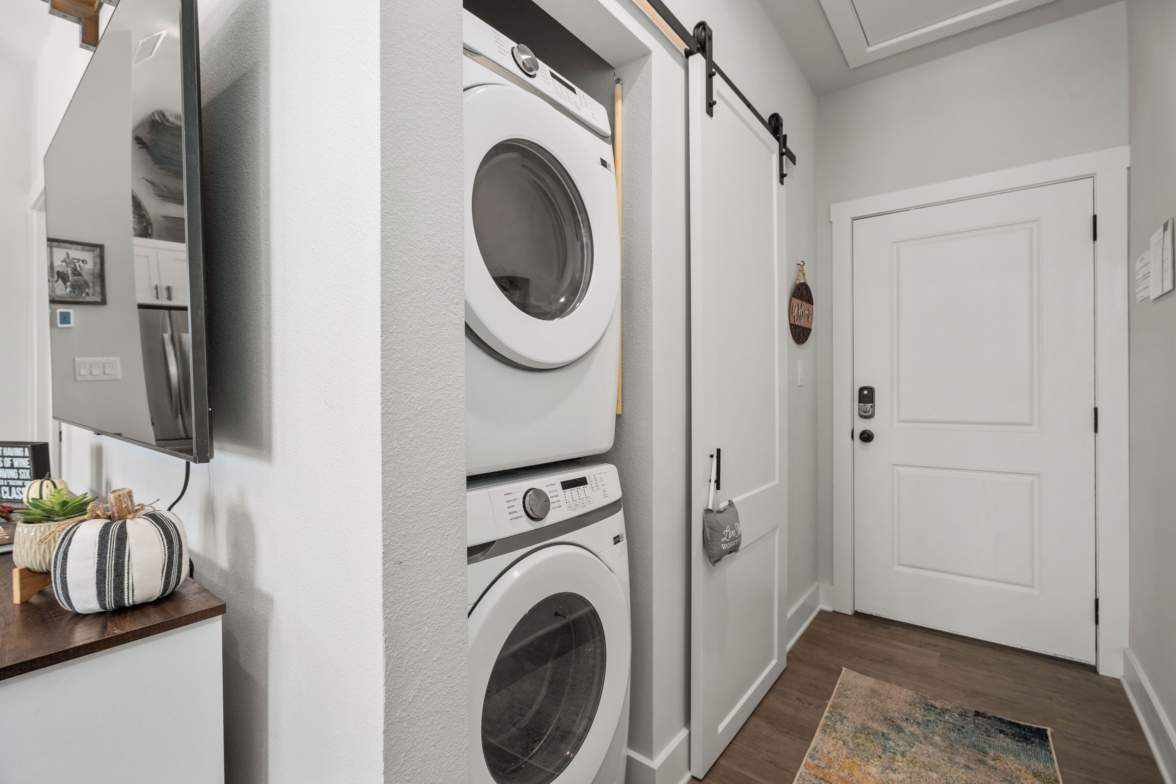 A laundry room with stacked washers and dryers, a wooden counter with decorative items, a mounted television, and a white door.