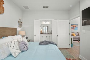 A bedroom with a bed, bedside table, lamp, and a view into the bathroom through an open door. - UnWine'd | Brand New | Hot Tub | Romantic (Fredericksburg)