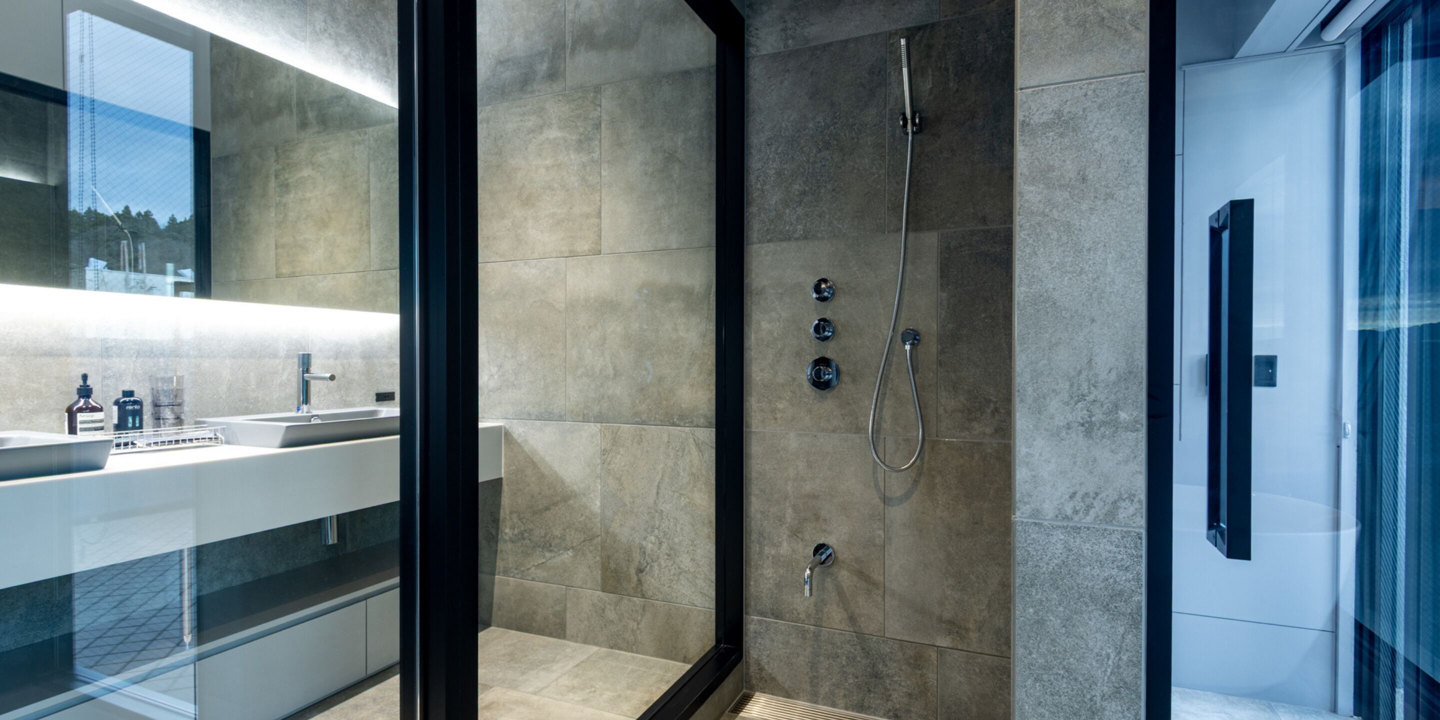 A modern bathroom with a glass shower enclosure, a sink with a mirror, and a countertop with toiletries.
