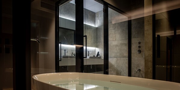 Un baño moderno con una bañera independiente, un box de ducha con paredes de vidrio y un espejo grande que refleja el ambiente.