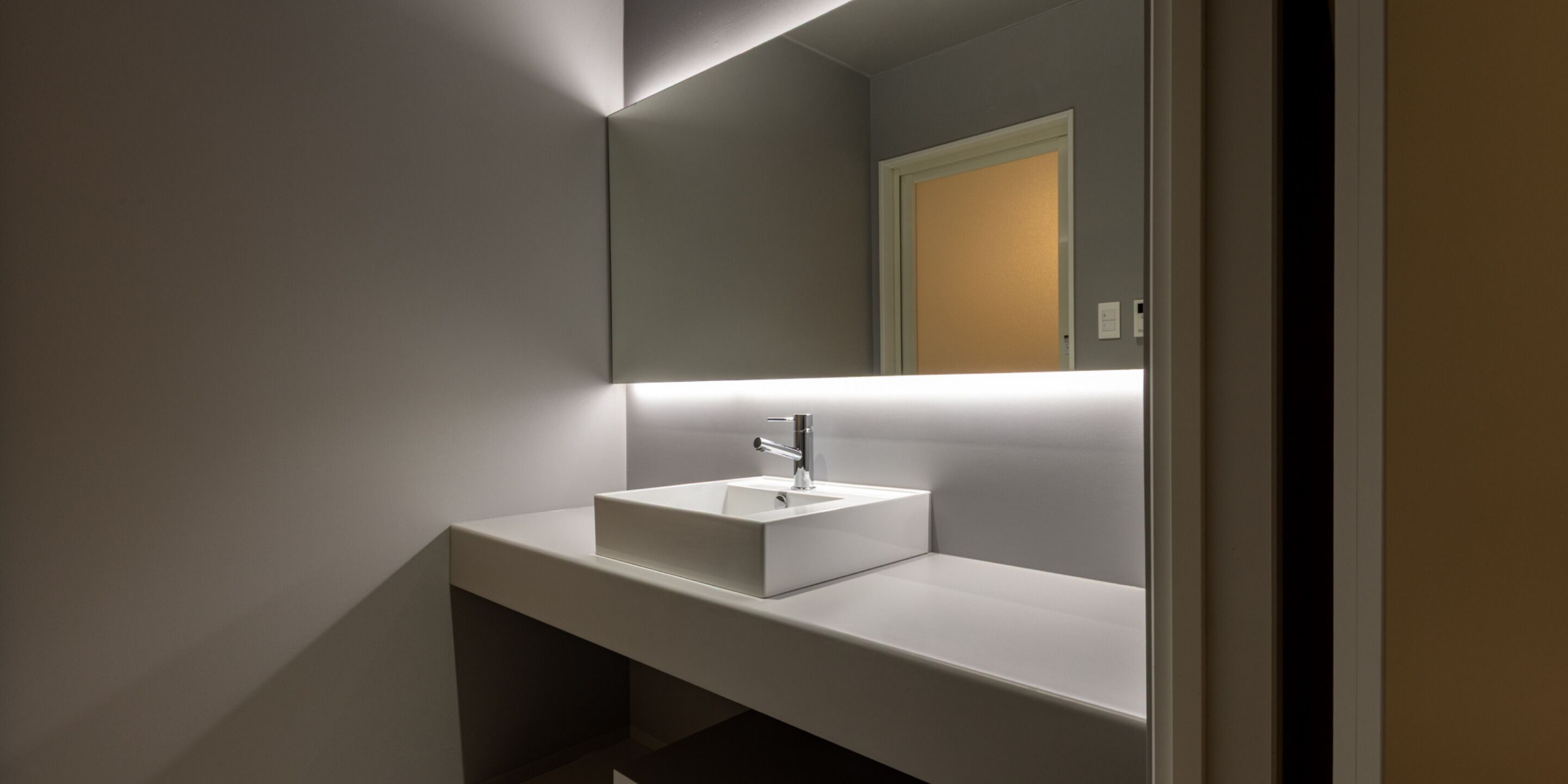 A modern bathroom with a white sink, a mirror, and a light above the sink.