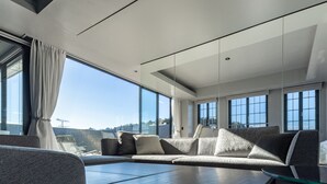 A modern living room with large windows, a sectional sofa, and a glass coffee table. - asuwagawaritoa-to asunowa (Fukui)