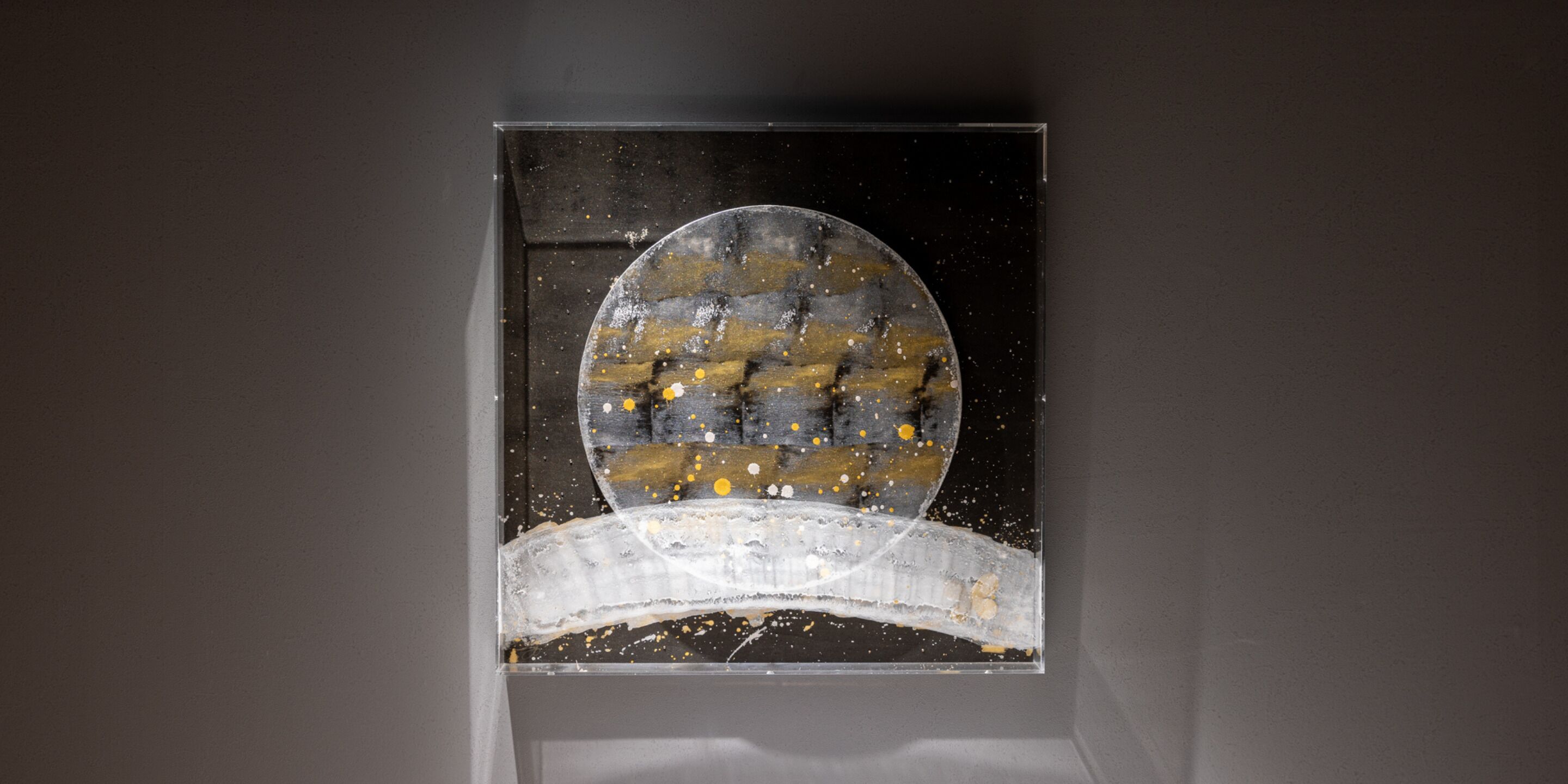 A framed artwork with a circular central piece and a curved base, set against a dark background.