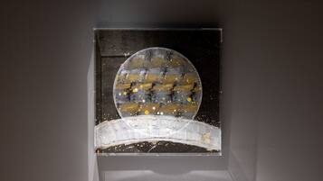 A framed artwork with a circular central piece and a curved base, set against a dark background.