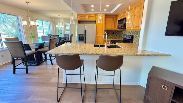 A modern kitchen with a central island, bar stools, wooden cabinets, and a large window. - Easy Access Lower Unit + Golf Views + Festival Location (La Quinta)