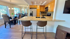 A modern kitchen with a central island, bar stools, wooden cabinets, and a large window. - Easy Access Lower Unit + Golf Views + Festival Location (La Quinta)