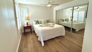 A bedroom with a bed, a nightstand, a lamp, a ceiling fan, and a large mirror. - Easy Access Lower Unit + Golf Views + Festival Location (La Quinta)