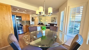 A modern kitchen with wooden cabinets, a stainless steel refrigerator, and a glass dining table with chairs. - Easy Access Lower Unit + Golf Views + Festival Location (La Quinta)