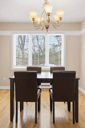 A dining area with a table and chairs, a chandelier, and a window with blinds. - Executive 7 Bedrooms 3 5 Bathrooms (Bedford)