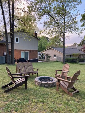 Ein Garten mit einem Feuerkorb, zwei Adirondack-Stühlen und einem Ziegelhaus.