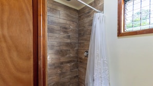 Una doccia con piastrelle di legno, una tenda bianca e una finestra con un motivo a griglia.