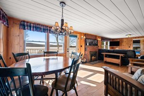A wooden interior with a dining table, chairs, a fireplace, a sofa, and a TV. - The Peninsula | Waterfront | Pet Friendly | Snowmobile Access (Rangeley)