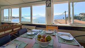 A dining area with a table set for two, a bowl of fruit, and a view of the sea and mountains. - 1 bedroom amazing apartment in Nafpaktos (Nafpaktos)