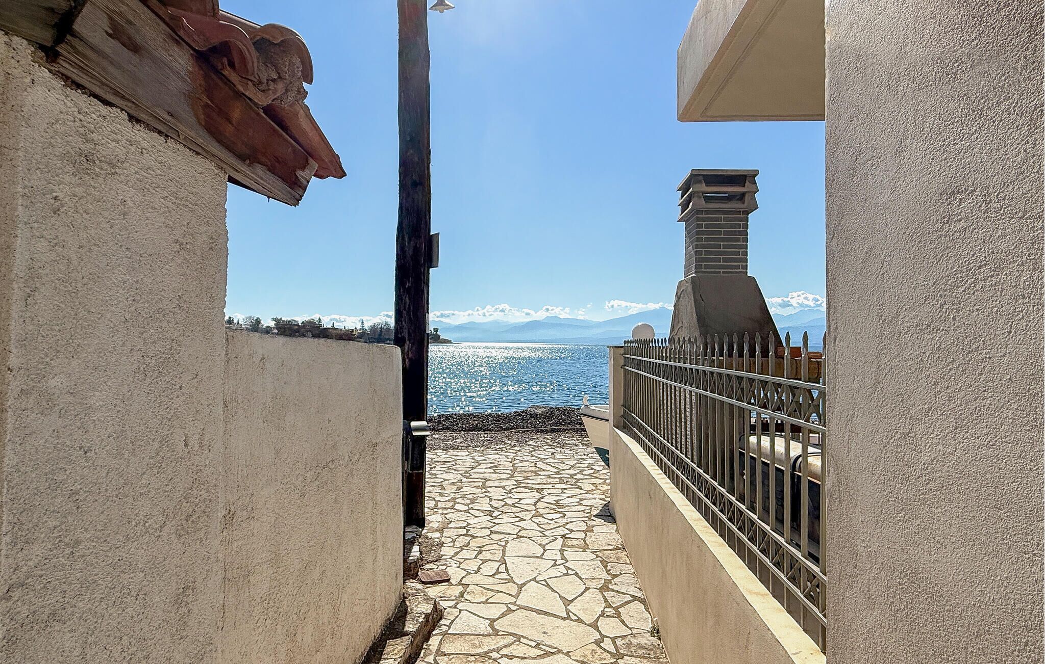 Un chemin de pierre mène à un balcon qui donne sur une étendue d’eau, avec des montagnes visibles au loin.