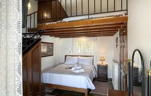 Une chambre à coucher avec un lit en bois, une table de chevet, une commode, un miroir et un escalier.