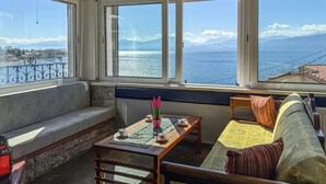 A room with a view of the sea and mountains, a bench, a table with a vase and cups, and a sofa with a cushion. - 1 bedroom amazing apartment in Nafpaktos (Nafpaktos)