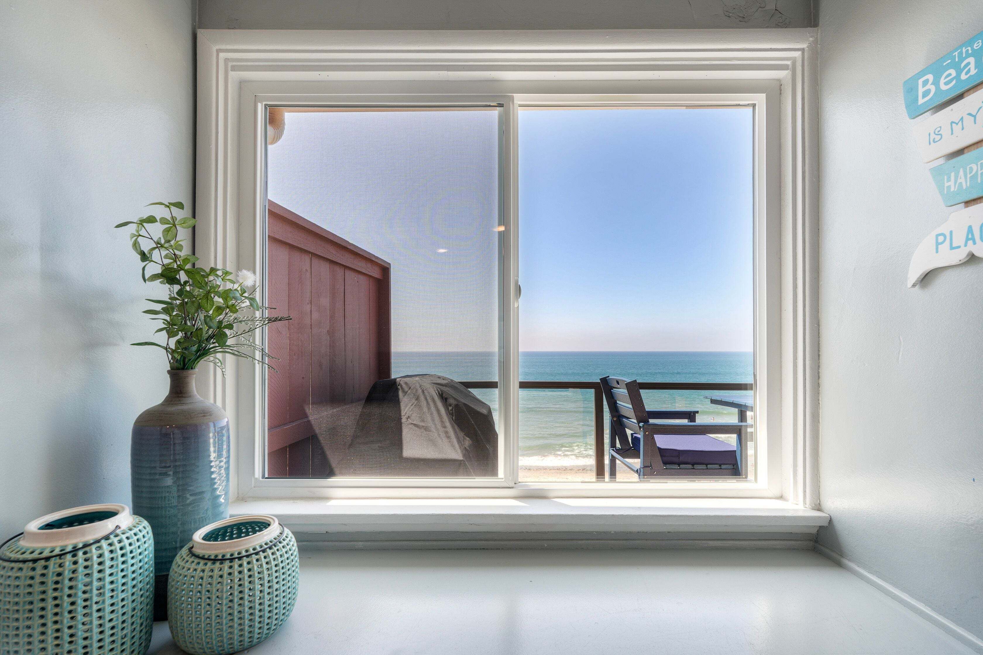 A window with a view of the ocean, a wooden deck, and a bench.