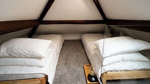 Una piccola e accogliente camera da letto in mansarda, con due letti singoli, travi a vista in legno e una porta vetrata che dà su un balcone.