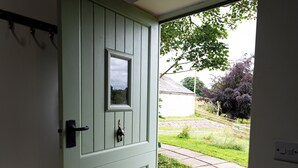 Una porta verde con una piccola finestra, un tappetino d'ingresso e un vialetto in pietra che conduce all'esterno.