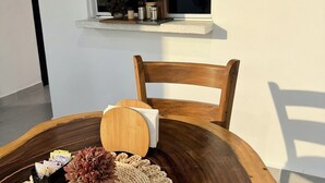 A round wooden table with a woven placemat, a vase with dried flowers, and a small container of currency. A wooden chair is positioned behind the table. - Surf City Private 7 Suite Hotel with AC + hot water (Conchalio)