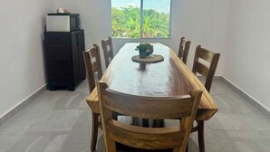A dining area with a wooden table and chairs, a small potted plant, and a view of greenery through a window. - Surf City Private 7 Suite Hotel with AC + hot water (Conchalio)