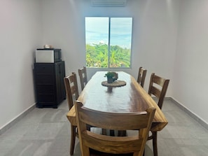 Un coin repas avec une table et des chaises en bois, une petite plante en pot et une vue sur la verdure par la fenêtre.