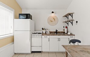 A compact kitchen with white cabinets, a stove, a microwave, a sink, and a dining table.