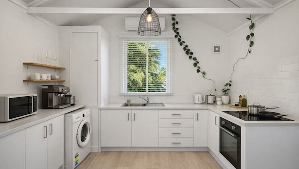 A modern kitchen with white cabinets, a built-in washing machine, a microwave, a coffee maker, and a stove.