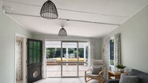 A spacious room with a sliding glass door leading to an outdoor patio, a grey sofa, a wooden rocking chair, and a black pendant light.