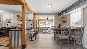 Une cuisine spacieuse avec des poutres en bois, un coin repas avec une table et des chaises en bois, et une grande fenêtre donnant sur l’extérieur.