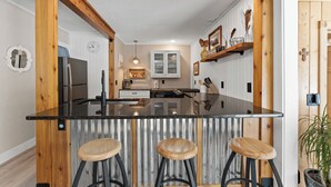Une cuisine dotée d’un îlot central, de tabourets de bar, de poutres en bois et d’une porte blanche.