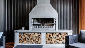 A fireplace with a stone facade, wood storage below, and wicker furniture.
