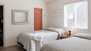 Un dormitorio con dos camas, una ventana con persianas, una puerta y un espejo en la pared.