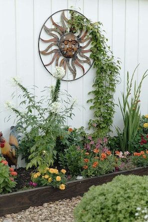 Un jardín con un adorno de sol metálico, diversas plantas y flores.